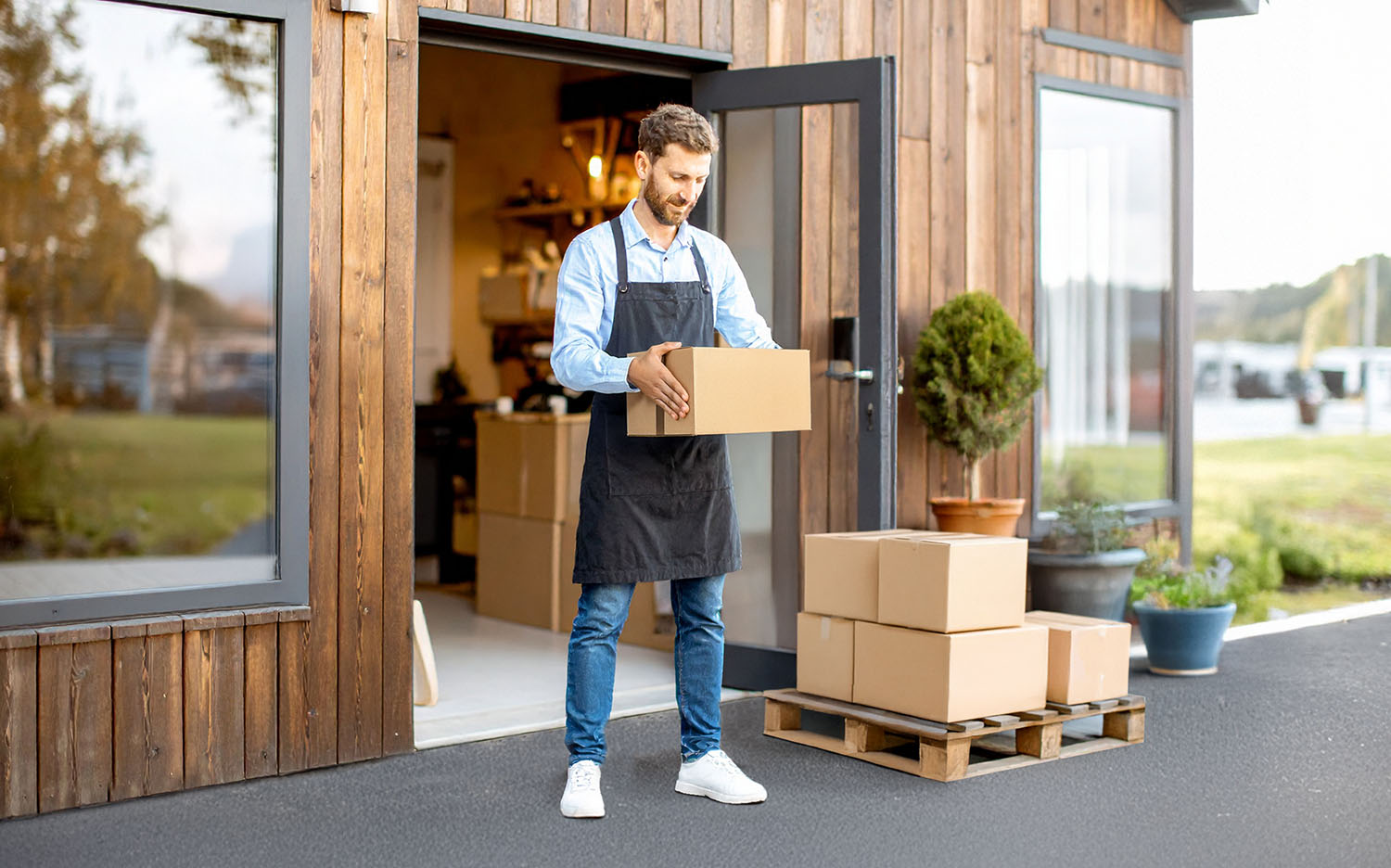 Man shop owner in front of a shop with parcel and pallet